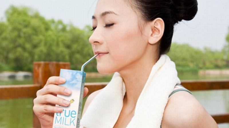Một ly sữa TH True Milk ít đường đặt trên bàn gỗ cùng các loại trái cây tươi và hạt dinh dưỡng